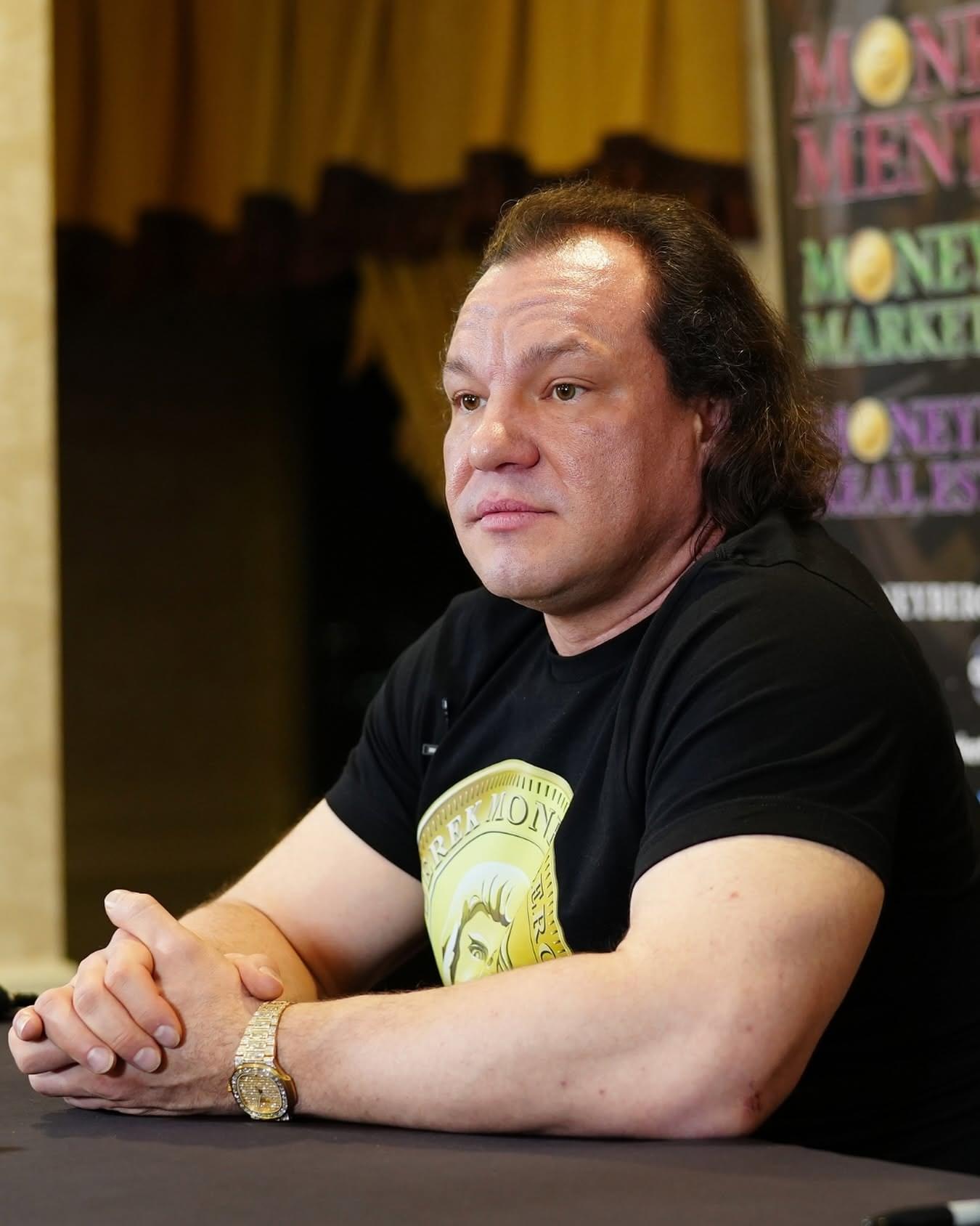 Derek Moneyberg seated at a table in a black Moneyberg shirt